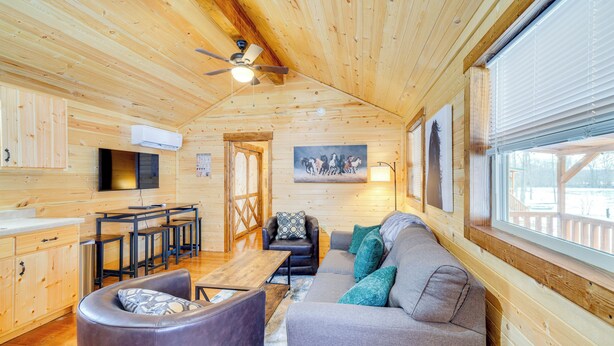 A log cabin interior with a wooden ceiling, a ceiling fan, a dining area with a table and chairs, a sofa with cushions, and a painting on the wall. - La Grange Cabin on a Racehorse Farm w/ Pond Views! (La Grange)
