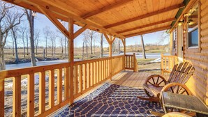 A wooden porch with a patterned rug, wooden chairs, and a view of a rural landscape. - La Grange Cabin on a Racehorse Farm w/ Pond Views! (La Grange)