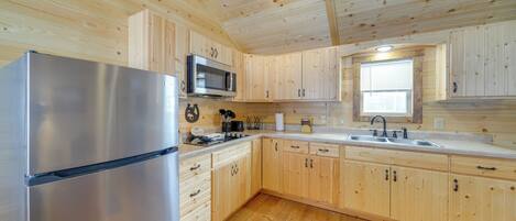 A modern kitchen with wooden cabinets, a stainless steel refrigerator, a microwave, and a sink.