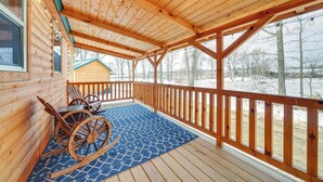 Una baita di legno con veranda coperta, una poltrona a dondolo e un tappeto azzurro con motivo decorativo.