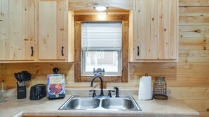 Una cucina con mobili in legno, un lavello doppio, un tostapane, un bicchiere e un sacchetto di pane.