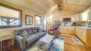 A cozy cabin interior with a sofa, armchair, wooden floors, and a kitchen area. - 31 Mi to Louisville: Cabin on 235 Acres! (La Grange)