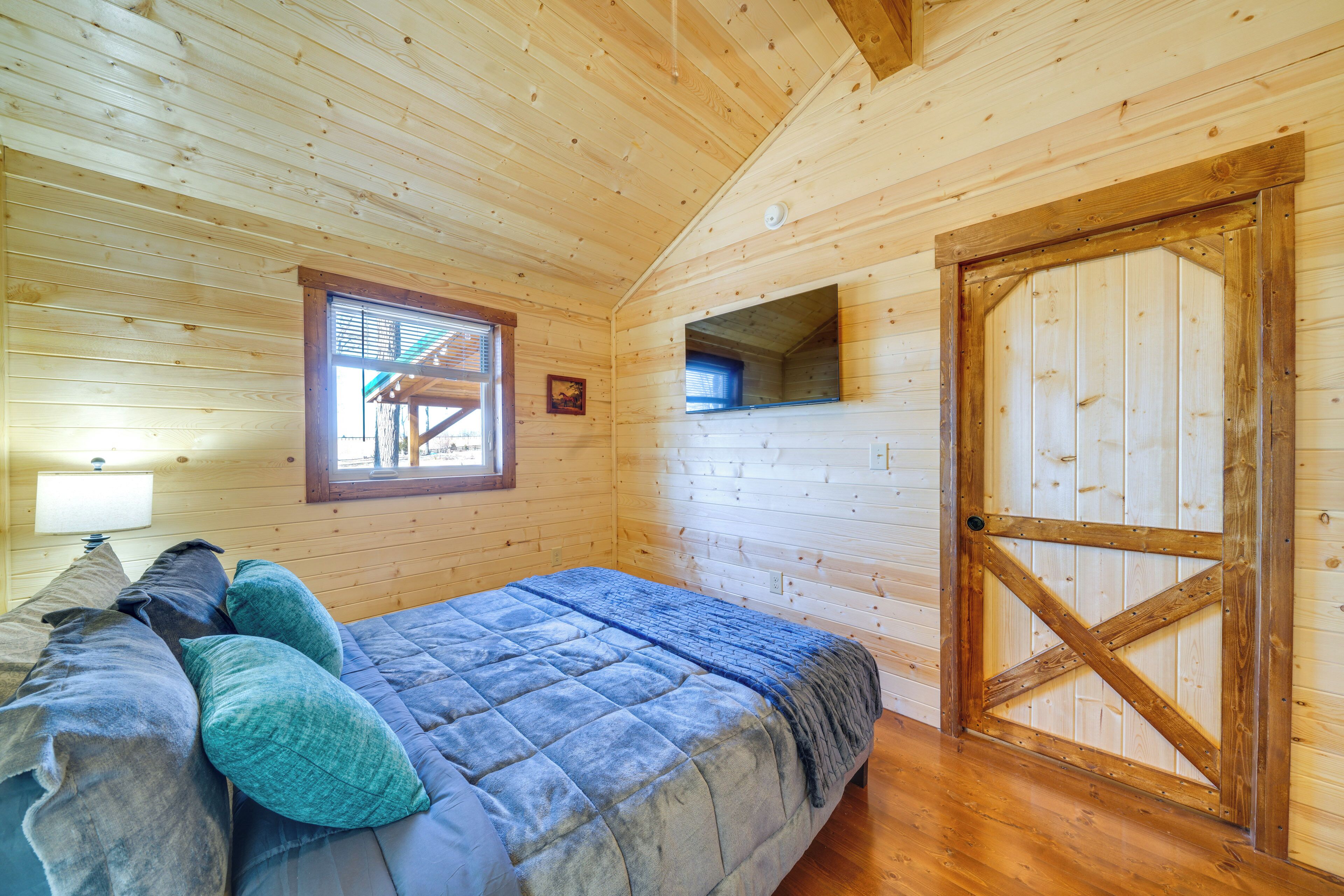 A wooden cabin bedroom with a bed, pillows, a window, and a door.