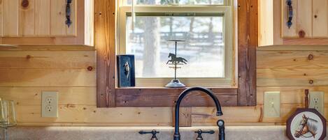 A kitchen with wooden cabinetry, a double sink, and a window with a decorative horse silhouette.