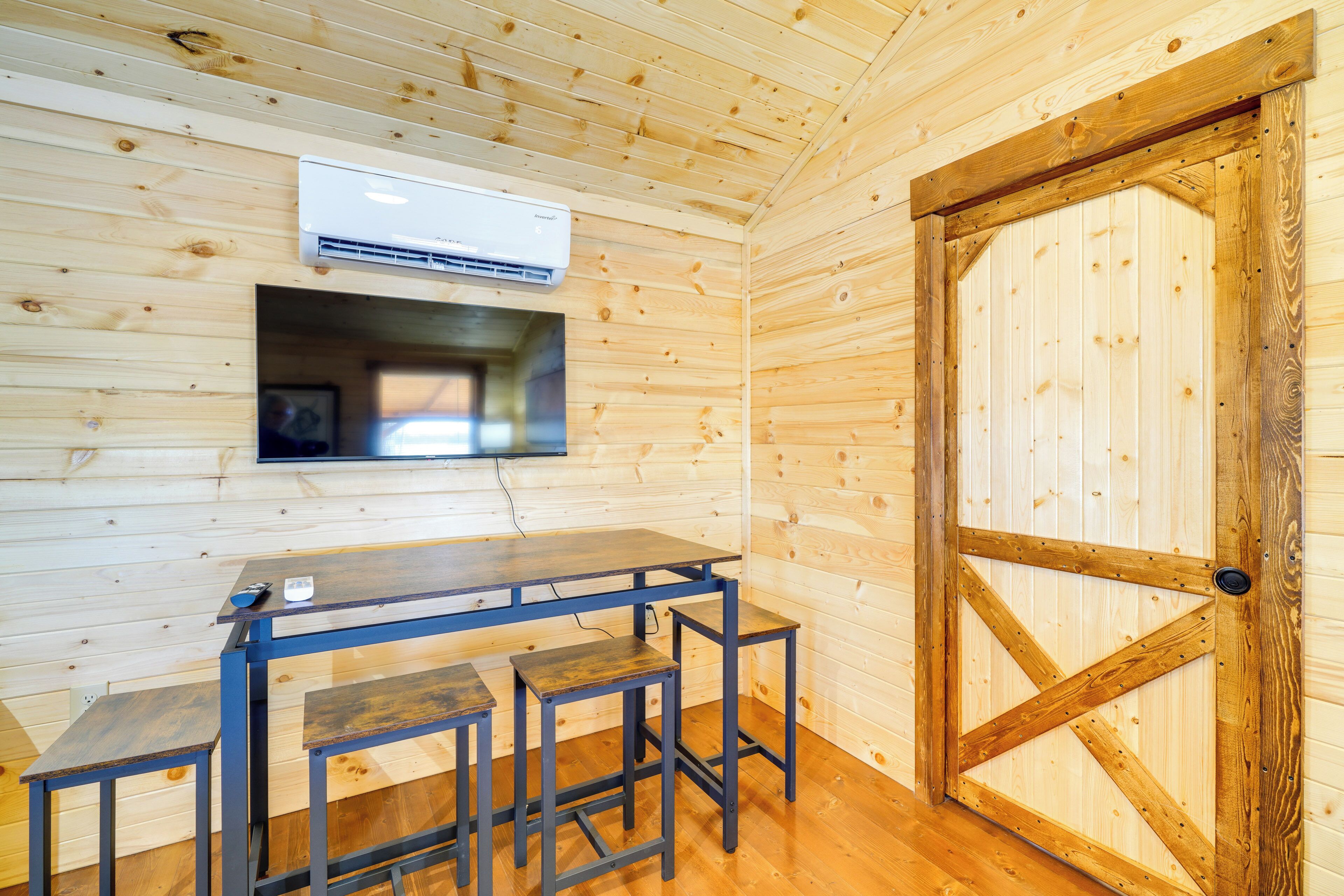 Un intérieur en bois avec une table et des tabourets, un appareil de climatisation et une porte en bois.
