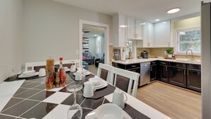 A modern kitchen with white cabinets, a dining area with a checkered tablecloth, and a view into a living room. - < 2 Mi to Ecu: Cozy Greenville Getaway w/ Porch! (Greenville)