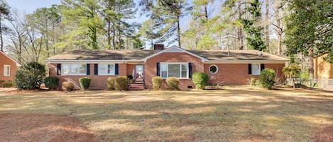 A single-story brick house with a front porch, surrounded by a well-maintained lawn and trees.