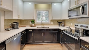 A modern kitchen with white cabinets, black appliances, and a window above the sink. - < 2 Mi to Ecu: Cozy Greenville Getaway w/ Porch! (Greenville)