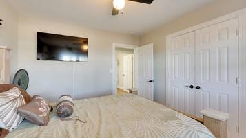 A bedroom with a bed, pillows, a ceiling fan, a wall-mounted TV, and a white door.