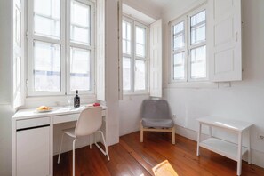 Une pièce avec un bureau blanc, une chaise, une petite table et une fenêtre donnant sur un paysage agréable.