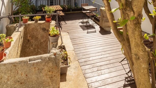 Een binnenplaats met een houten terras, plantenpotten en een boom.