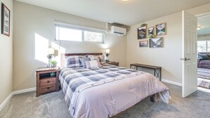 Un dormitorio con cama, mesitas de noche, ventana y aire acondicionado.