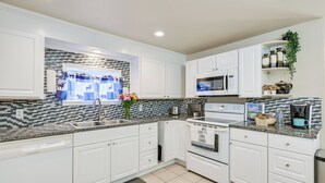 Una cocina moderna con armarios blancos, encimera de granito, microondas integrado y cafetera.
