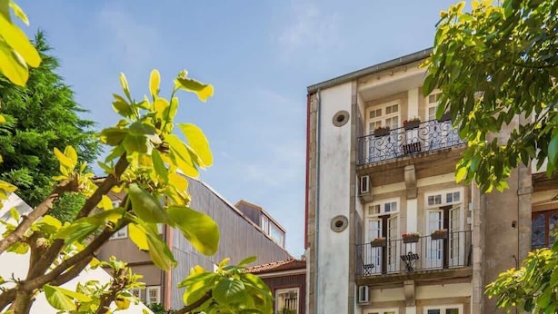 A courtyard with wooden tables and chairs, a stone wall, and a building with balconies. - Porto Lounge Hostel - Cozy Bed in Mixed Dorm (Porto)