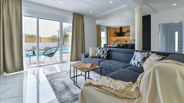 Ein modernes Wohnzimmer mit einer Couch, einem Couchtisch und Blick auf einen Außenpool.