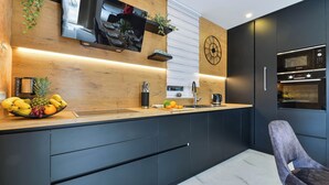 Eine moderne Küche mit Holzauszug, schwarzen Schränken, einem eingebauten Ofen und einem Fernseher, der über der Arbeitsfläche angebracht ist.