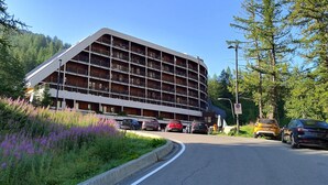 A multi-story building with balconies, surrounded by lush greenery and parked cars. - Myka Cervinia Apartment - lovely studio apartment in Breuil Cervinia (Breuil-Cervinia)