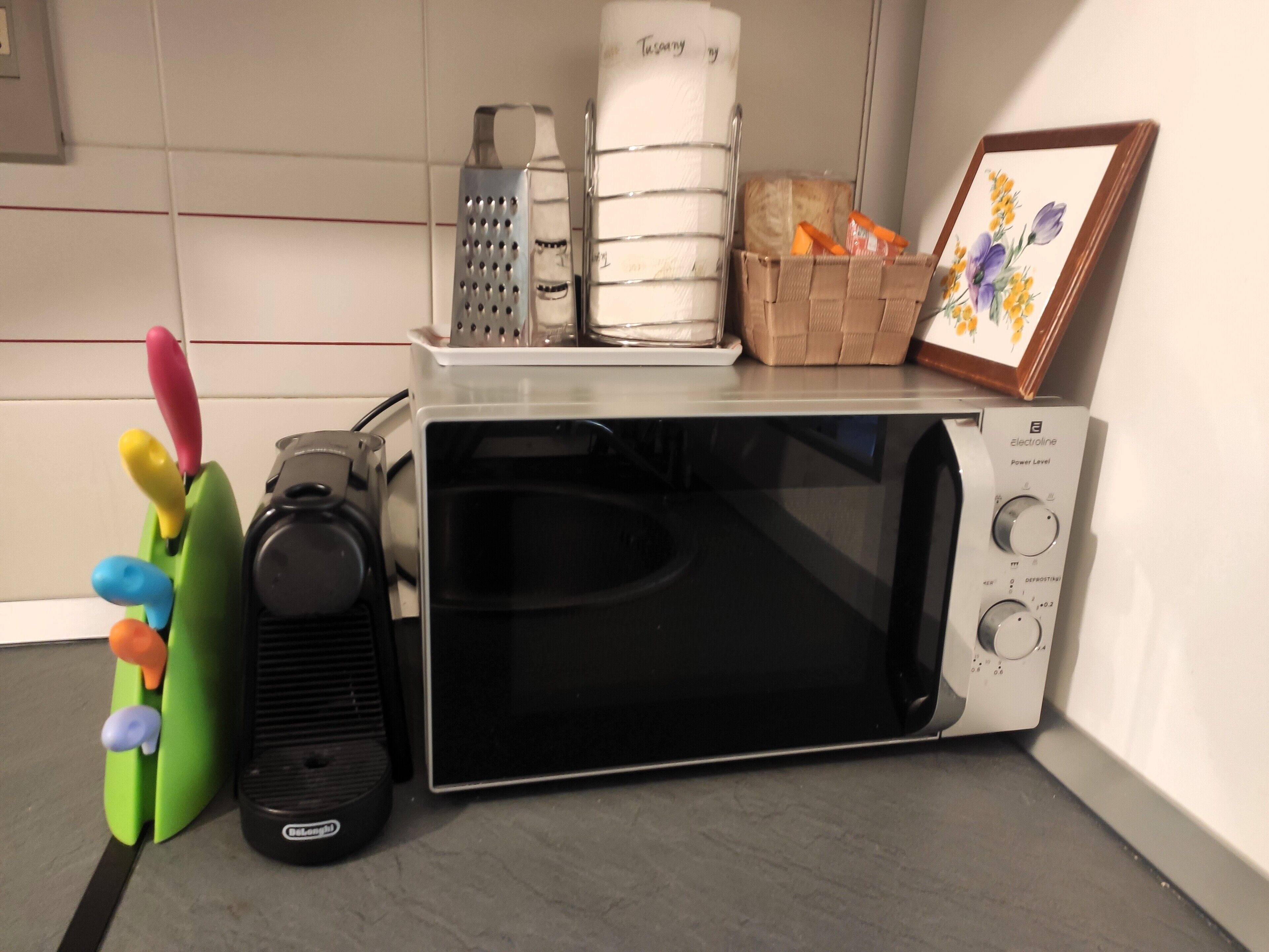 A kitchen with a microwave, toaster, and a toaster with a green handle. There are also some utensils and a picture frame on the counter.