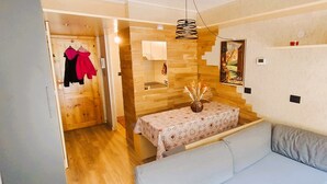 A room with a wooden floor, a bed with grey bedding, a table with a patterned tablecloth, and a wall with a poster. - Myka Cervinia Apartment - lovely studio apartment in Breuil Cervinia (Breuil-Cervinia)