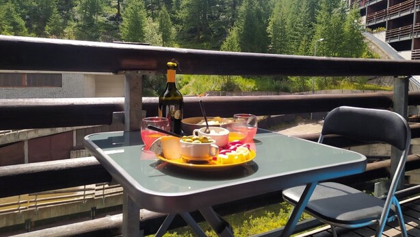 A table with a bottle, glasses, and a fruit platter on a balcony overlooking a forest. - Myka Cervinia Apartment - lovely studio apartment in Breuil Cervinia (Breuil-Cervinia)