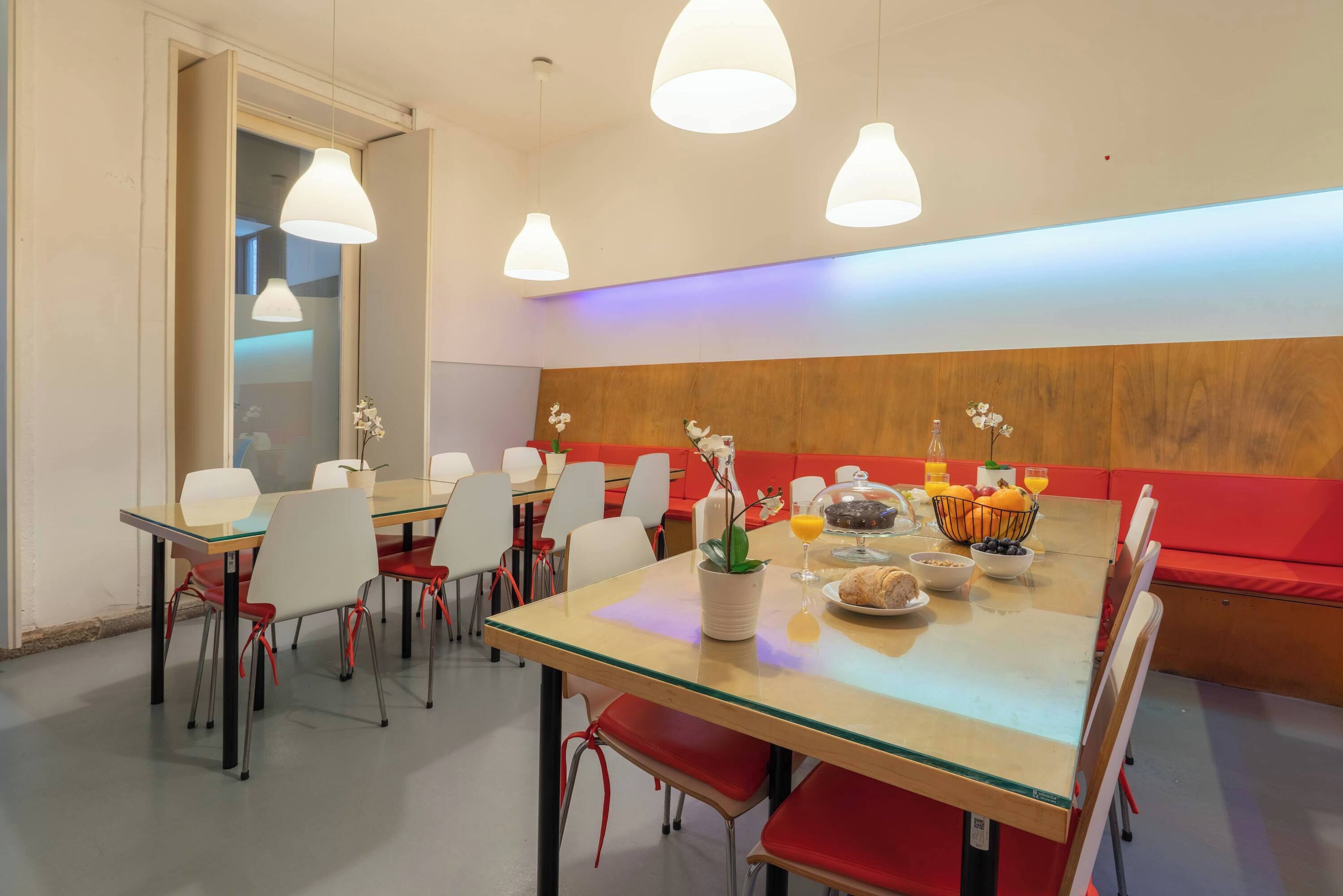 Un comedor con una mesa de vidrio, sillas rojas y blancas, y una pared de madera.