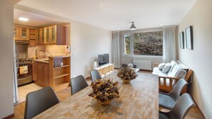 A modern kitchen with wooden cabinets, a dining table with chairs, and a living area with a sofa and a TV. - Spacious Central Apartment with Garage (San Carlos de Bariloche)