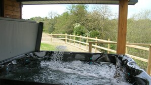 Un jacuzzi con chorros de agua, terraza de madera y vistas a árboles y una valla.