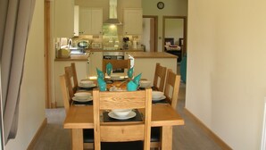 Un comedor con una mesa de madera dispuesta para cuatro personas, sillas y una cocina al fondo.