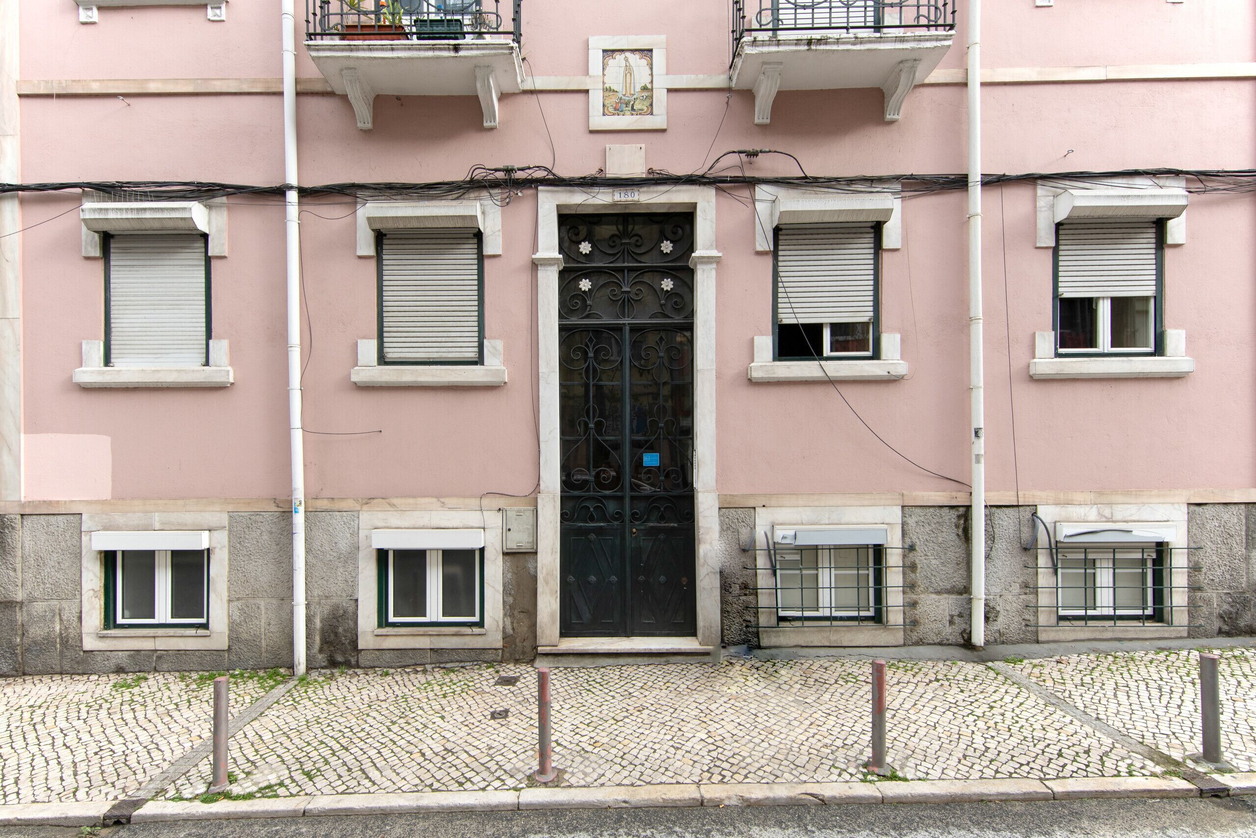 A pink building with a black door, multiple windows with shutters, and a cobblestone street.