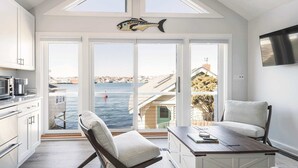 A modern kitchen with white cabinets, a dining area with a table and chairs, and large windows offering a view of the sea and buildings. - Stay at Rocky Neck (Gloucester)