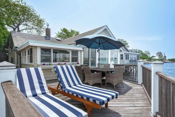 A wooden deck with two striped lounge chairs and a table with wicker chairs.