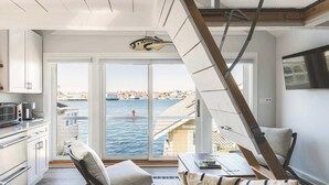 A modern kitchen with white cabinets, a dining area with a table and chairs, and a large window overlooking a body of water. - Stay at Rocky Neck (Gloucester)