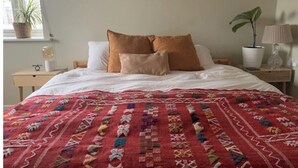 A neatly made bed with a red patterned bedspread, two white pillows, and a brown accent pillow. - Airy one-bed in Limehouse with views of the city (London)