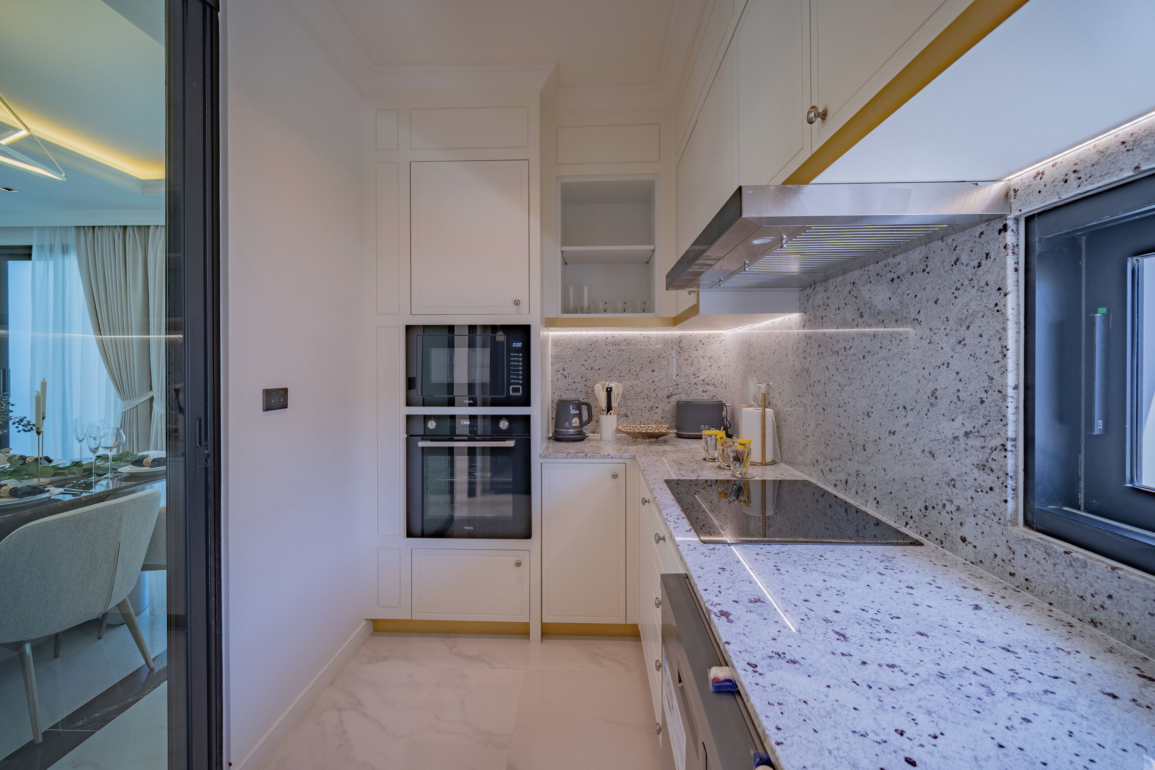 A modern kitchen with white cabinetry, a built-in oven, and a granite countertop.