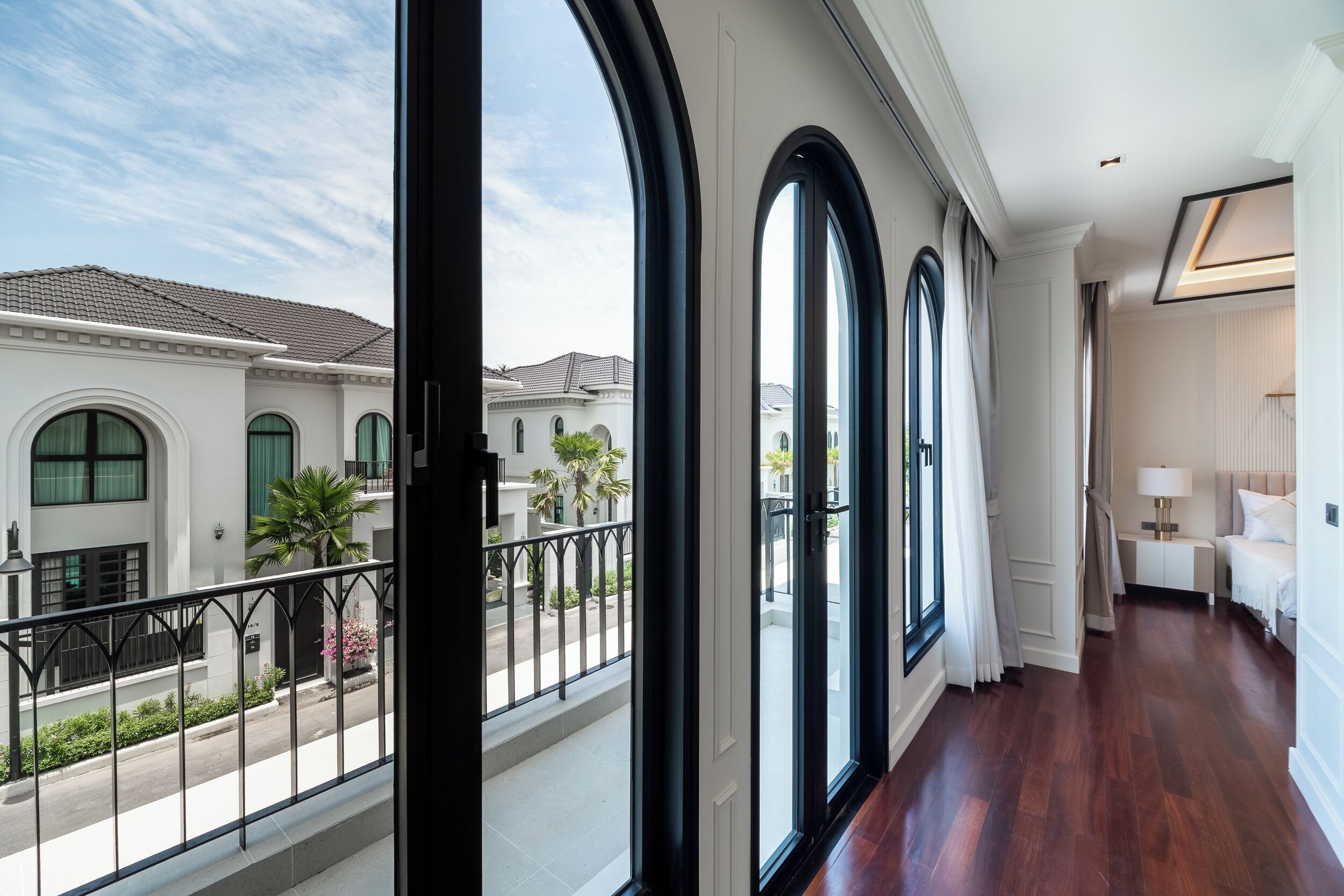 A hotel room with large arched windows, a balcony, and a view of neighboring buildings.