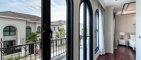 A hotel room with large arched windows, a balcony, and a view of neighboring buildings.