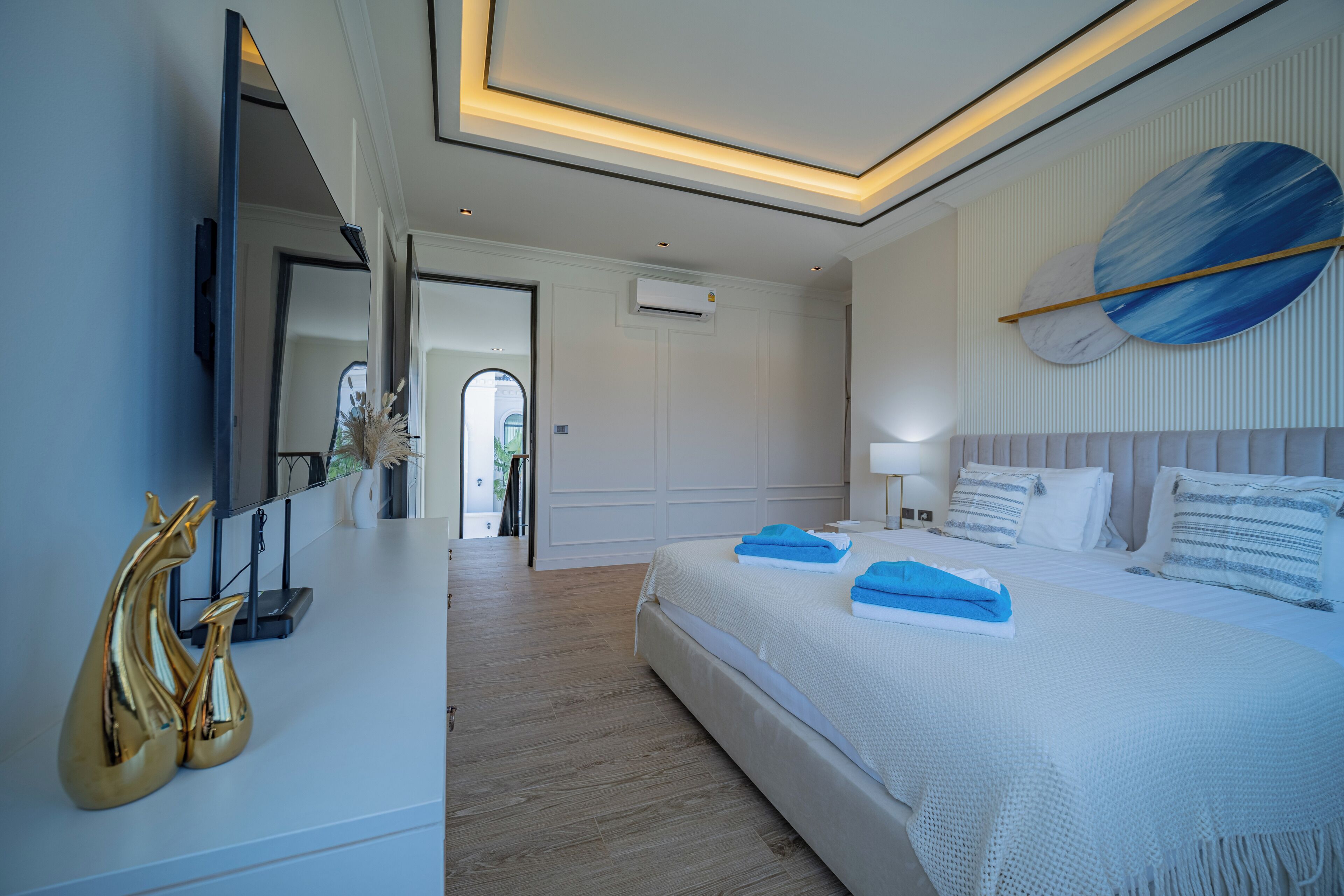 A modern bedroom with a large bed, bedside tables, a flat-screen TV, and a ceiling light fixture.