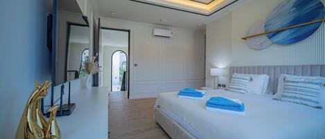 A modern bedroom with a large bed, bedside tables, a flat-screen TV, and a ceiling light fixture.