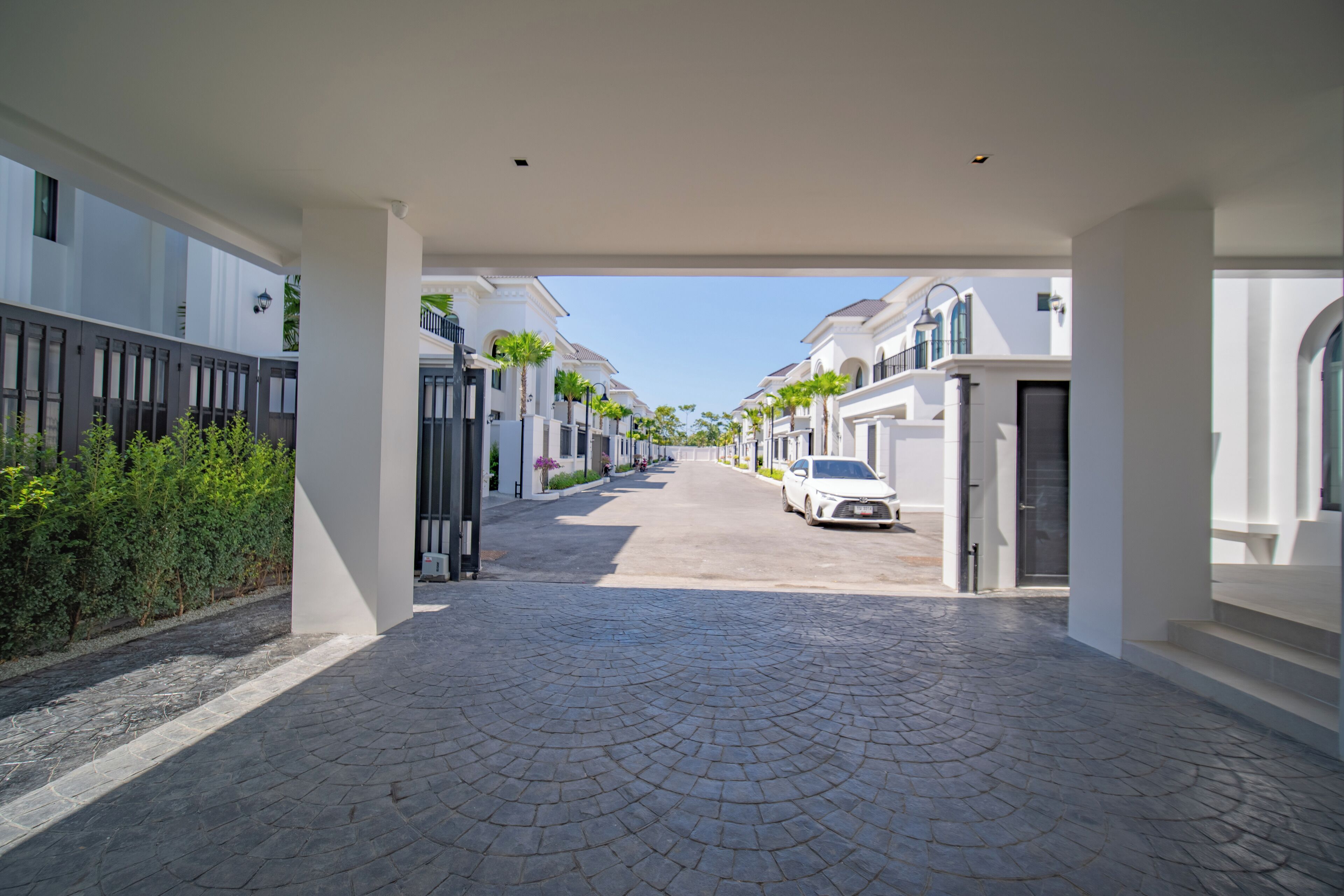 A paved pathway leading to a white building with a car parked in front.
