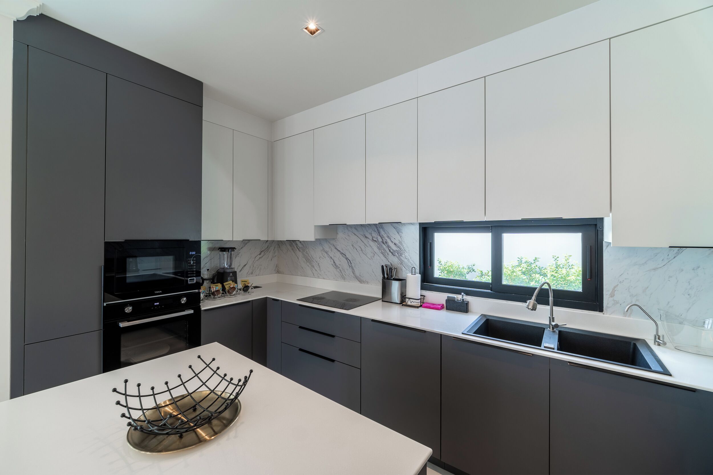 Une cuisine moderne avec des meubles de couleur sombre, un micro-ondes noir et une fenêtre au-dessus de l’évier.