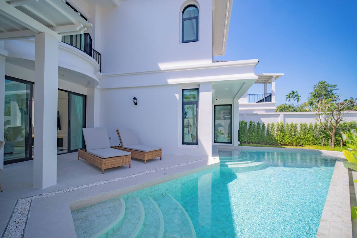Une maison moderne dotée d’une piscine, d’une façade blanche et d’un balcon aménagé avec des meubles en osier.