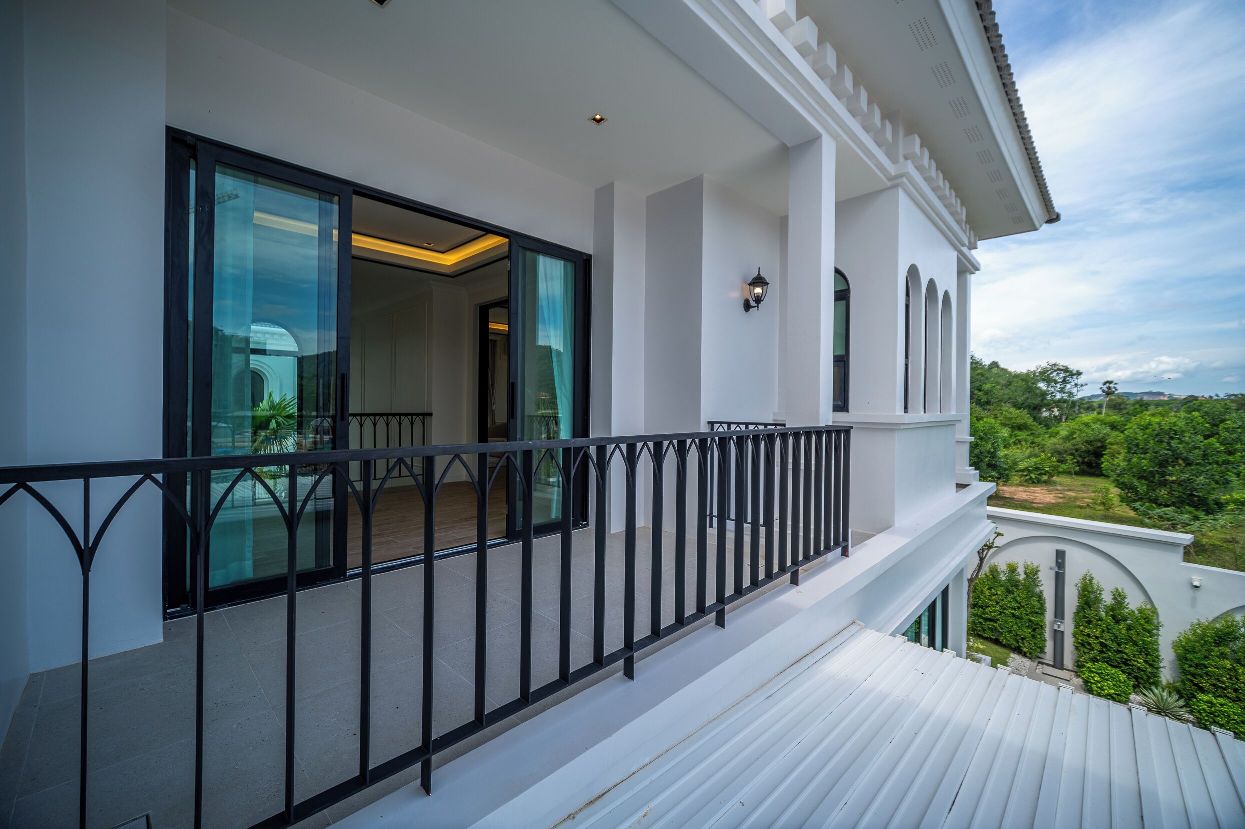 A modern house with a balcony, large windows, and a view of greenery.