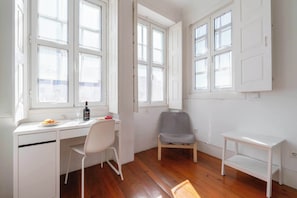 A room with a white desk, a chair, a small table, and a window with a view.