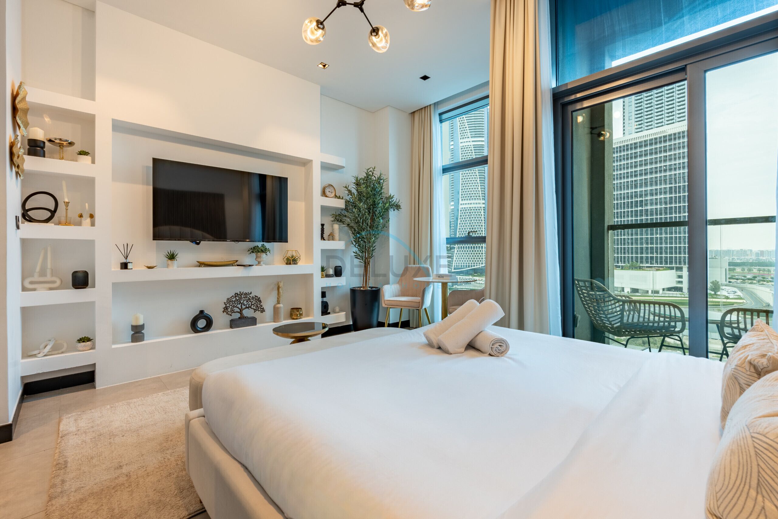 Una habitación de hotel moderna con una cama grande, televisión integrada y un balcón con vistas a la ciudad.