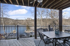 Une terrasse couverte, dotée d’une table et de chaises, qui offre une vue sur un lac et sur des bâtiments situés au loin.
