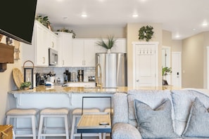 A modern kitchen with white cabinets, stainless steel appliances, and a bar area with stools.