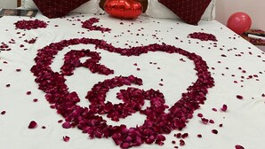 A bed with rose petals arranged in a heart shape, a red balloon, and a painting with the word "love" on the wall. - PURPLE PETAL HOTEL (Rohtak)