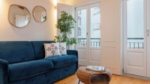 A living room with a blue sofa, a wicker ottoman, wooden beams on the ceiling, and a potted plant. - Stylish Retreat in Porto's Heart by HostWise (Porto)
