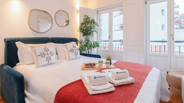 A hotel room with a bed, a red blanket, a tray with food, and towels with the 'hostwise' logo. - Stylish Retreat in Porto's Heart by HostWise (Porto)
