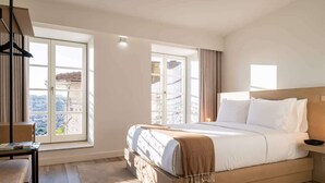 A modern hotel room with a large bed, a desk, and a view of the city through large windows. - 5 Fervença Boutique Palace Flats by HostWise (Vila Nova de Gaia)